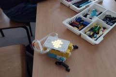 Na stoliku leży włączony robot. Posegregowane klocki lego znajdują się w białym pudełku.