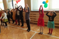 Dzieci z podniesionymi rękami tańczą na sali gimnastycznej.