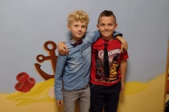 Dwóch chłopców przy kolorowej ścianie, jeden trzyma rękę na ramieniu drugiego