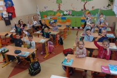 Dzieci siedzące e szkolnych ławkach i pokazujące otrzymane upominki