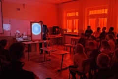 Drupa osób w zaciemnionej sali, mężczyzna pokazuje na ekranie świecące koło