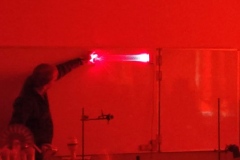 Na białej tablicy wyświetla się laserowy napis, który nauczyciel wskazuje palcem