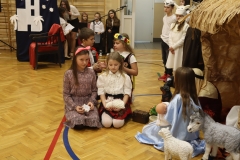 Grupa dzieci klęczy przed szopką