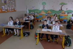 Uczniowie siedzący w ławkach szkolnych i obserwujący to, co się dzieje na ekranie