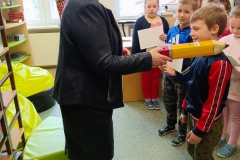Uśmiechnięty chłopiec przed panią dyrektor, która ołówkiem pasuje go na czytelnika szkolnej biblioteki