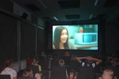 Grupa dzieci siedzi w kinie  i ogląda film.