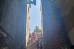 Dzieci schodzą wąskim korytarzem po schodach na dół w tle niebo, mury z cegły.