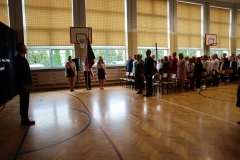 Nauczyciel stoi przed zgromadzonymi na sali gośćmi w czasie wykonywania hymnu