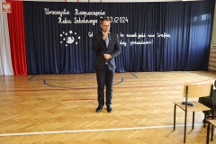 Na tle dekoracji stoi mężczyzna w ciemnym garniturze