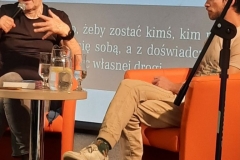 Na zdjęciu widać Janka Melę I Marka Kamińskiego. Obaj siedzą na pomarańczowych fotelach, pan Marek trzyma w ręku mikrofon.