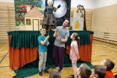 Aktor prezentuje kukiełkę, obok niego stoi dwójka dzieci