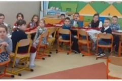 W sali lekcyjnej na krzesłach siedzi grupa dzieci