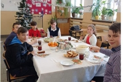Uśmiechnięci chłopcy i jedna dziewczynka siedzą przy stoliku, na którym leżą paszteciki, owoce i napoje