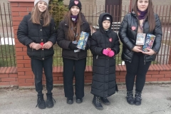 Cztery dziewczyny ubrane na czarno stoją przy ogrodzeniu kościelnym. Dwie z nich trzymają puszki WOŚP